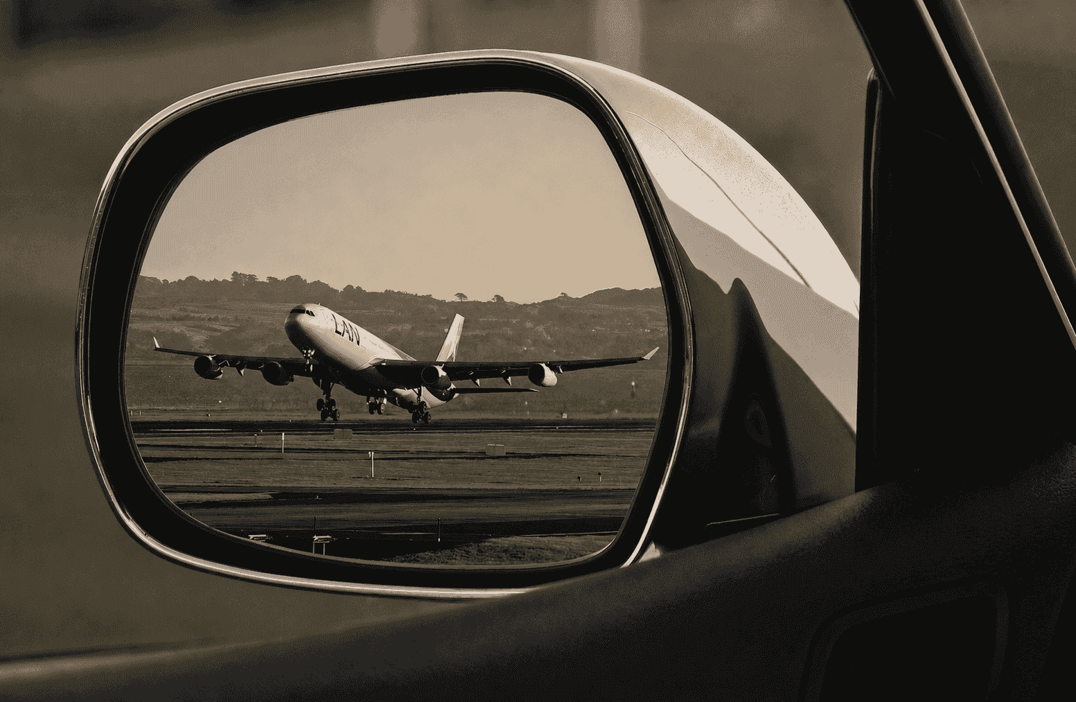 Aereo in decollo riflesso nello specchietto retrovisore di un'auto NCC all'aeroporto di Milano Linate.
